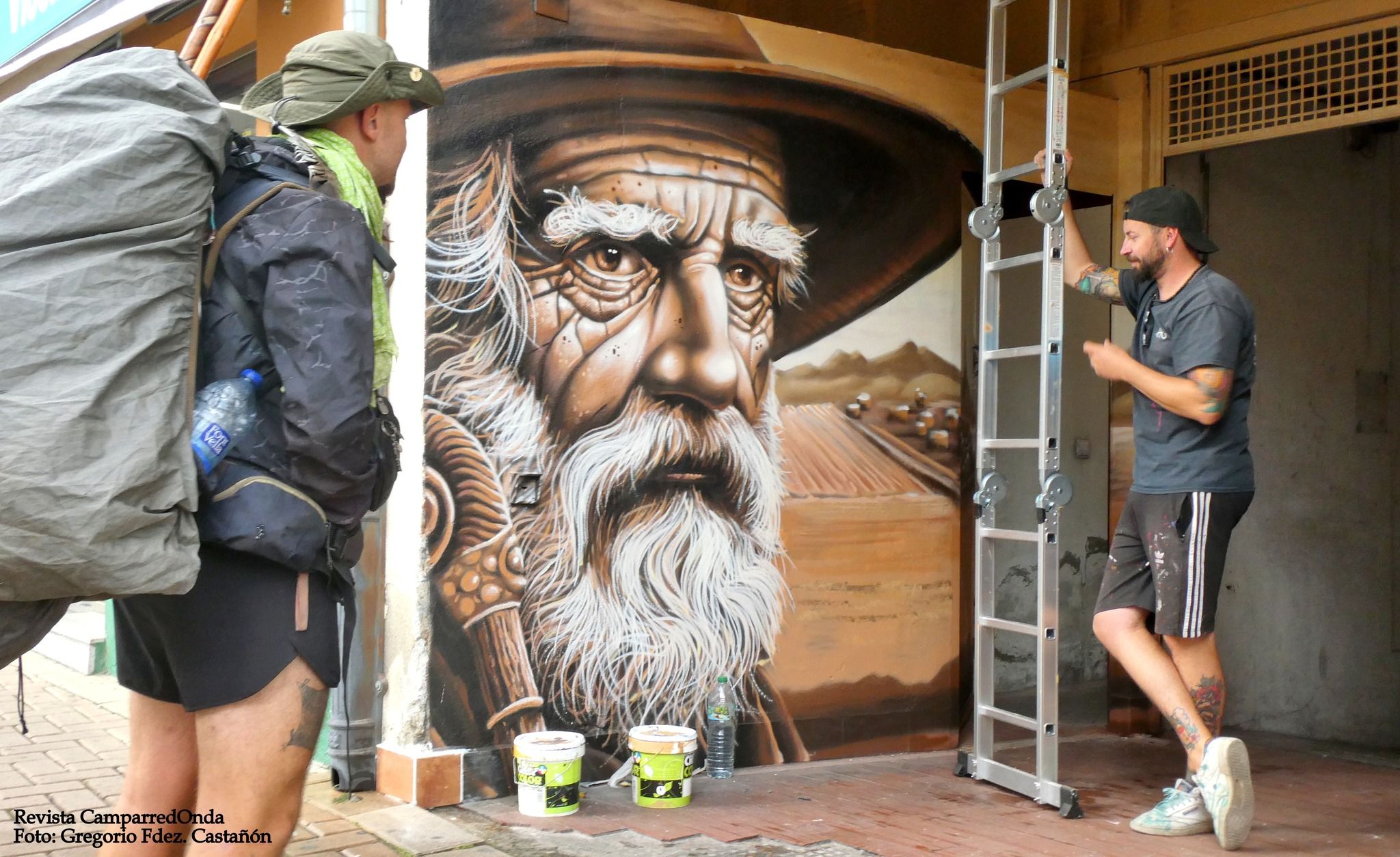 Un peregrino y Toño Prada junto a su nuevo mural en la capital provincial. | GREGORIO FERNÁNDEZ CASTAÑÓN (REVISTA CAMPARREDONDA)