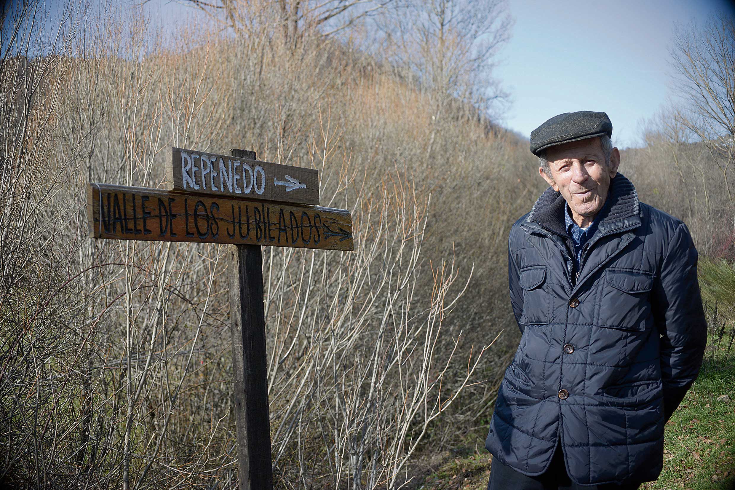 Elías Rodríguez, Tío Elías, posa orgulloso ante dos de los carteles que él mismo hizo, uno con una  broma, ‘El valle de los jubilados’.| MAURICIO PEÑA