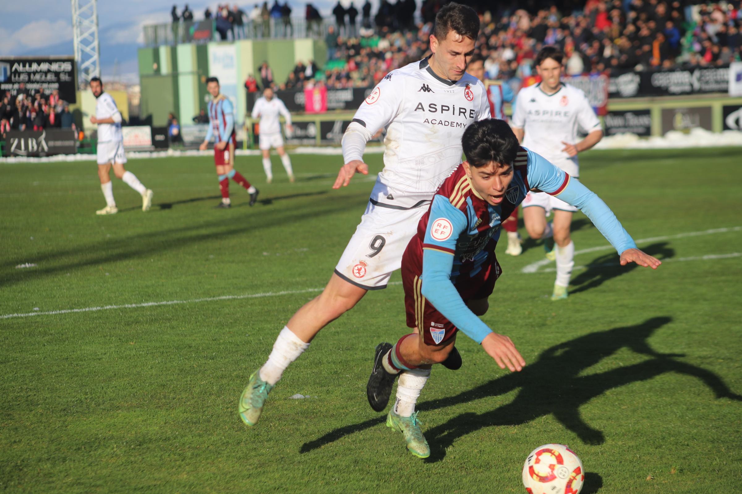 El delantero de la Cultural Manu Justo derriba a un jugador de la Segoviana. | ISAAC LLAMAZARES